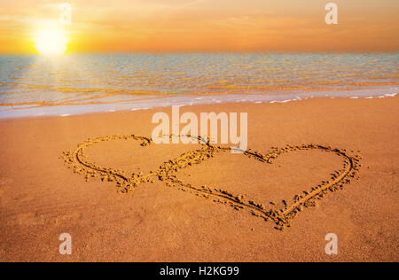 zwei hand gezeichnete Herzen am Strandsand über Sonnenuntergang Stockfoto