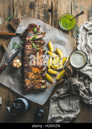 Geröstete Schweinerippchen mit Knoblauch, Rosmarin, grüner Kräutersauce, Bratkartoffeln und dunkles Bier auf rustikalen hölzernen Hintergrund, Draufsicht, ver Stockfoto