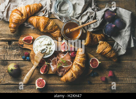 Frühstück mit frisch gebackenen Croissants, Ricotta-Käse, Feigen, frische Beeren, Prosciutto di Parma und Honig in Glas über ru Stockfoto