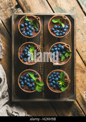 Hausgemachte Tiramisu Dessert in Gläser mit Zimtstangen, Minze und frische Heidelbeeren serviert in Holztablett über rustikale w Stockfoto