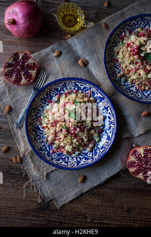 Couscous mit Kichererbsen, Mandeln und Granatapfel auf blauen Keramikplatten und rustikalen Holztisch Stockfoto