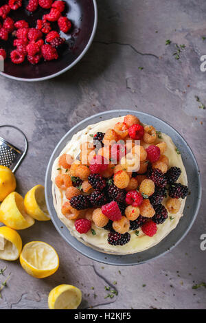 Biskuit mit Zitronencreme, dekoriert mit frischen bunten gelb rote Himbeeren und Dewberries, serviert auf graue Platte mit Thymian Stockfoto