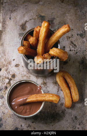 Traditionelle spanische Churros mit Schokolade Soße, serviert in Blechdose über alte strukturelle Metall Hintergrund zu behandeln. Draufsicht mit Kopie Stockfoto