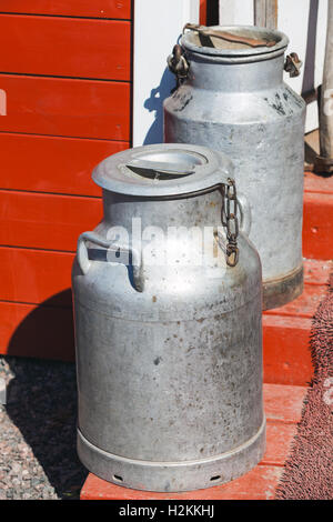 Zwei Metall Milchkannen stehen auf Holztreppen in der Nähe von ländlichen rote Wand Stockfoto