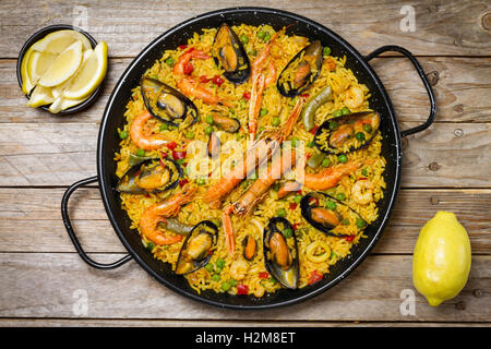 Spanische Paella auf einem Holztisch mit Zitrone in eine Schüssel geben und eine frische Zitrone Stockfoto