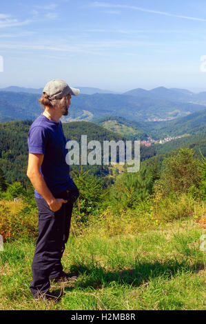 ein bärtiger Mann, Wanderer mit Rucksack, stehend in den Bergen und in die Ferne sieht. Hinten Sie Ansicht von. Sonniger Tag. Stockfoto