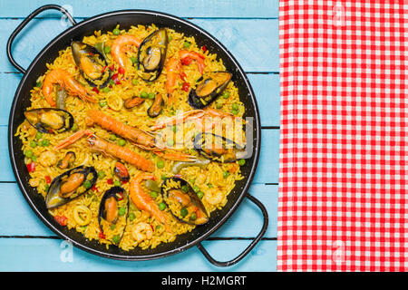 Spanische Paella und eine weiße und rote Tischdecke auf einem blauen Holztisch Stockfoto