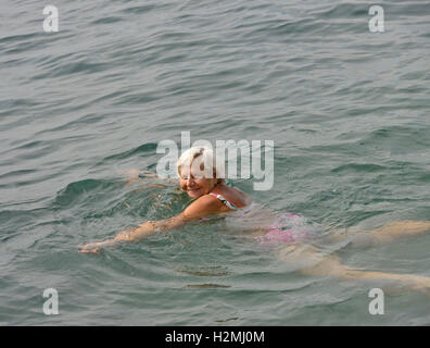 Alte Frau ist in hellen klaren Meerwasser angesichts Sonnenaufgang schwimmen. Stockfoto