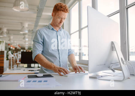 Aufnahme des jungen Mannes an seinem Schreibtisch stehen und arbeiten am Computer. Geschäftsmann, arbeiten in modernen Büros. Stockfoto