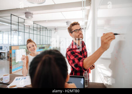 Lässige junge Geschäftsfrau, eine Präsentation auf Tafel und zu Kollegen erklären, während Meetings im Konferenzraum. Stockfoto