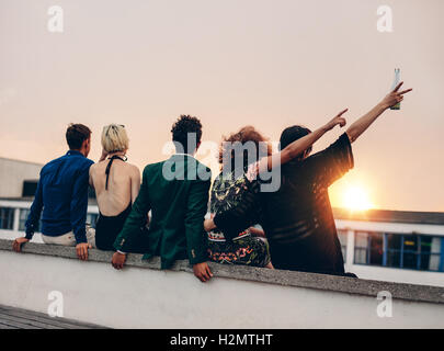 Gruppe von Freunden feiern auf Terrasse mit Getränken. Junge Männer und Frauen genießen Drinks auf der Dachterrasse bei Sonnenuntergang. Stockfoto