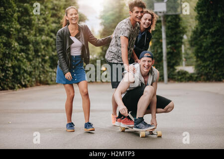 Voller Länge Schuss Teenager Jungs auf Skateboard mit Mädchen. Heterogene Gruppe von Freunde, die Spaß im Freien. Stockfoto