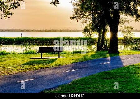 Eine Parkbank neben den Overholser Seenwegen. Eine einsame Frau geht auf dem Deich zwischen dem nordkanadischen Fluss und dem Overholser See. Oklahoma, USA. Stockfoto