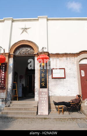 Ein chinesischer Mann nimmt ein Nickerchen vor dem Eingang zu einem offiziellen aussehende Gebäude in Tongli, eine Wasserstadt in Jiangsu, China. Stockfoto