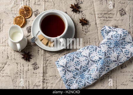 Tasse heißen Tee und kleine Milchkännchen auf dekorative Tischdecke Stockfoto