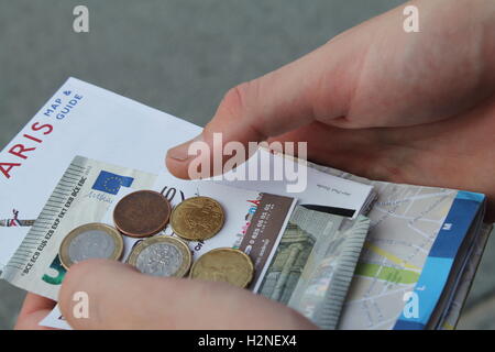 Hände halten ein Sortiment von Euro-Münzen, Noten und eine Karte und Reiseführer von Paris Stockfoto