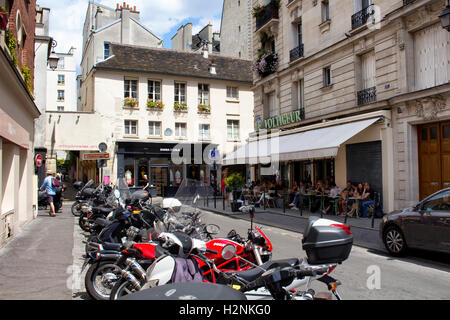 Menschen haben Mittagessen in einem der Restaurants in Le Marais Bezirk von Paris. Viele Motorräder parken auf der Straße. Stockfoto