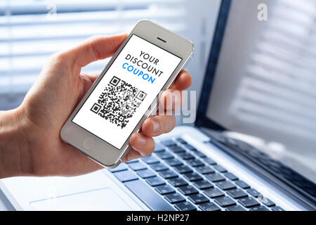 Rabatt-Coupon mit QR-Code auf Smartphone mit Laptop im Hintergrund Stockfoto