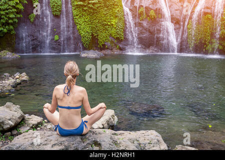 Mädchen üben von Yoga und Meditation im Lotussitz in der Natur in der Nähe eines Wasserfalls Stockfoto