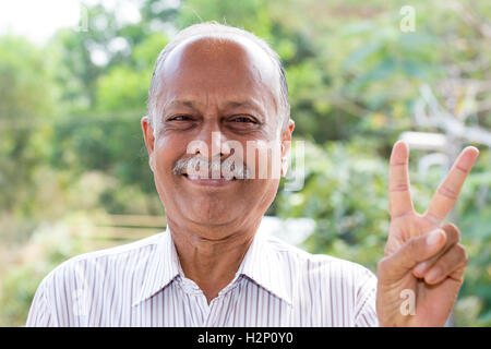 Closeup Portrait, freudige älterer Herr in weiß gestreiftes Hemd mit zwei Fingern, isoliert draußen im freien Hintergrund Stockfoto