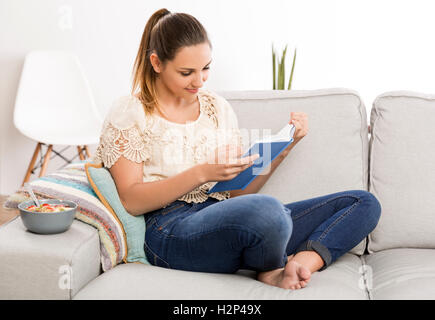 Schöne Frau zu Hause auf der Couch sitzen und ein Buch zu lesen Stockfoto