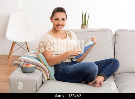 Schöne Frau zu Hause auf der Couch sitzen und ein Buch zu lesen Stockfoto