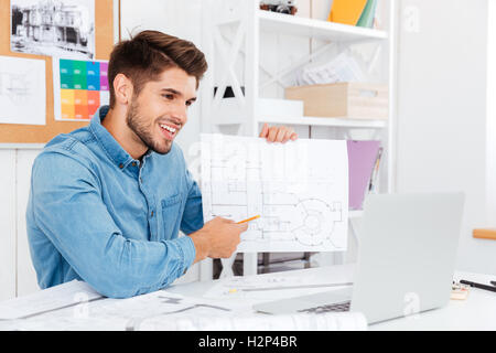 Lächelnde junge casual Geschäftsmann Dokumente auf einer Kamera anzeigen, während Sie sitzen im Büro Stockfoto