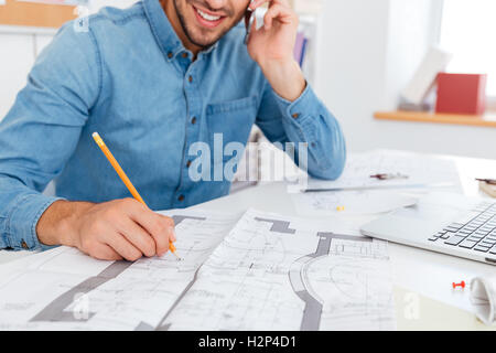 Bild eines lächelnden jungen Geschäftsmann telefonieren mit Handy und sich Notizen macht, während Sie im Büro sitzen abgeschnitten Stockfoto