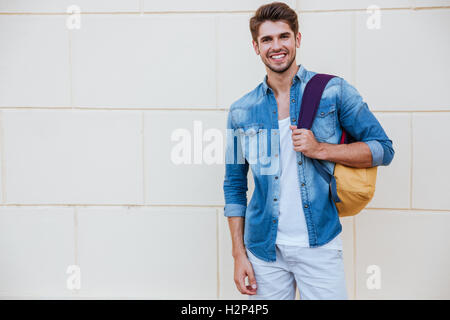 Porträt von fröhlichen jungen Mann mit Rucksack stehen und Lächeln Stockfoto