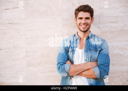 Fröhlichen jungen Mann stand mit verschränkten Armen Stockfoto
