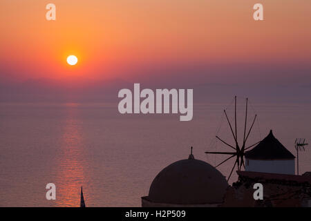 Blick auf den Sonnenuntergang in Oia, Santorini, Griechenland, mit Kirchenkuppel und Windmühle Stockfoto