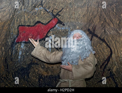 Der bärtige Einsiedler in Sackleinen zeigt Malerei Tiere an Höhlenwänden. Stockfoto