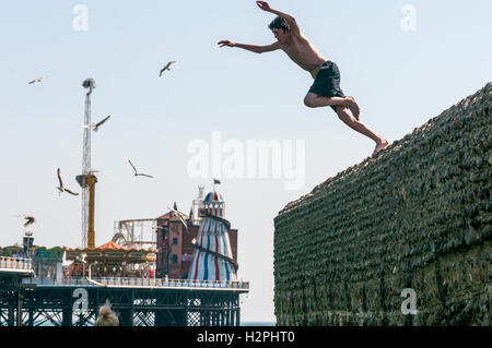Jugendliche aus Buhnen auf Brighton Beach ins Meer springen an einem heißen Nachmittag. Stockfoto