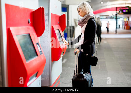 Frau mit Automaten am Bahnhof Zugticket kaufen Stockfoto