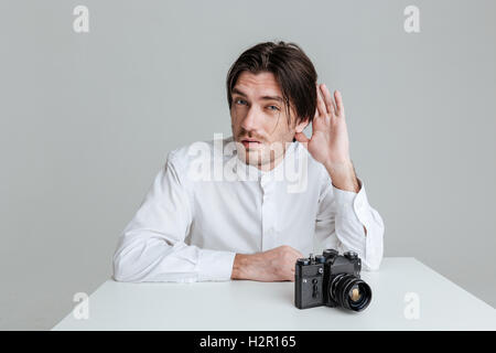 Junge Borsten Brünette Menschen das Gespräch beim Sitzen am Tisch isoliert auf den grauen Hintergrund belauscht Stockfoto