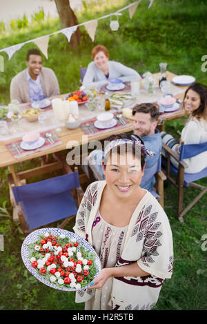 Lächelnde Frau Porträt dienen Caprese Salat mit Freunden am Tisch Gartenparty Stockfoto