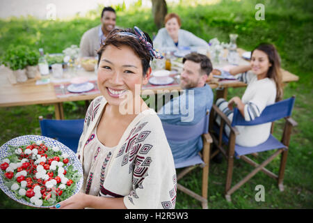 Lächelnde Frau Porträt dienen Caprese Salat mit Freunden am Tisch Gartenparty Stockfoto