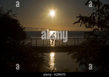 Swansea, Großbritannien. 2. Oktober 2016. UK-Wetter: Ein Radfahrer macht seinen Weg über die Fußgängerbrücke am Blackpill beim Sonnenaufgang über Swansea Bay heute Morgen. Bildnachweis: Phil Rees/Alamy Live-Nachrichten Stockfoto