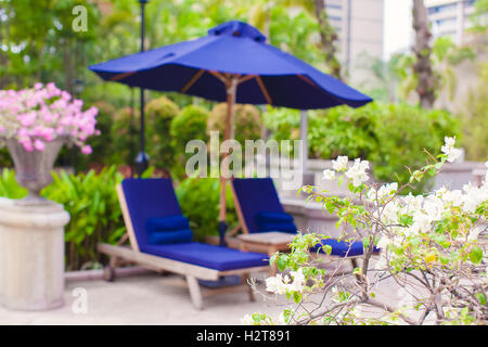 Zwei blaue Liegestühle mit Sonnenschirmen in der Nähe von Schwimmbad im Luxushotel Stockfoto