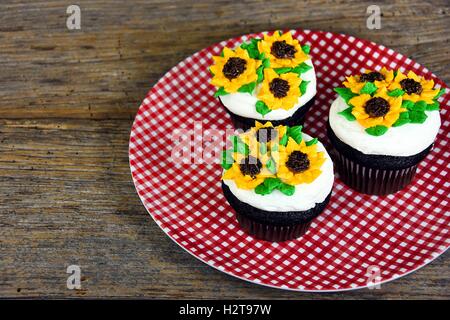 Sonnenblume Zuckerguss Design auf Schokoladentörtchen auf rot-weiß karierten Teller Stockfoto