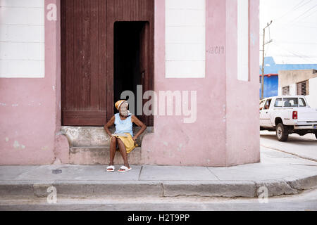 Eine kubanische Seniorin mit Essen auf der Straße; sitzen auf das Tor zu ihrem leichten rosa Haus in Santiago De Cuba, Kuba. Stockfoto