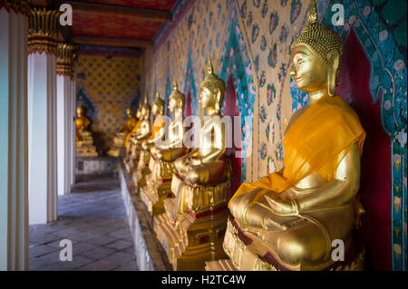 Reihe von Golden sitzenden Buddhas tragen gelbe Schärpe vor dekorative Wand in einem buddhistischen Tempel in Bangkok Thailand Stockfoto