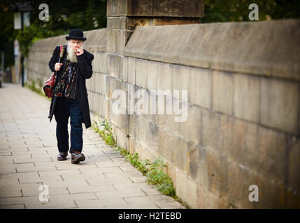 Lancaster Karikatur alte Mann Karikatur mit Melone zu Fuß über eine Brücke in die Innenstadt, dunkle schwarze Kleidung und Leder Tasche Hobo Stil Stockfoto