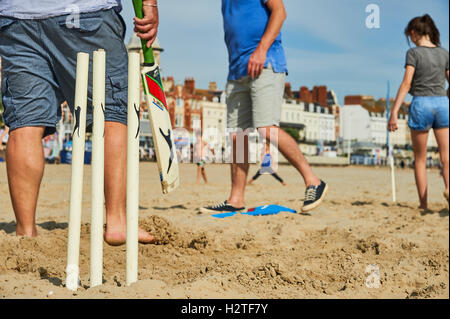 Familie und Freunde, die an einem sandigen Strand ein Strand-Cricket-Spiel genießen. Stockfoto