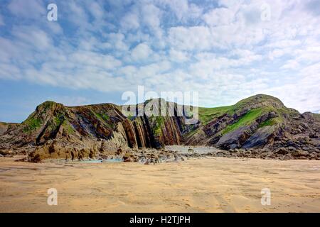 Detail der geologischen Schichten im küstennahen Klippen in der Nähe von Bude, England. Die Landschaftselemente gelben Sand, Rasen, Rock und blauer Himmel. Stockfoto