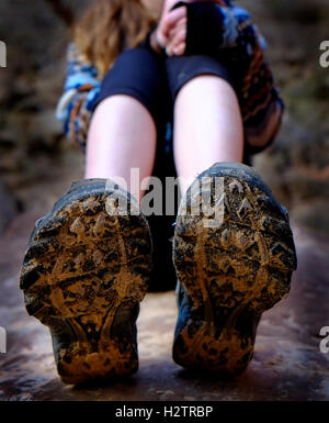 Junge Mädchen tragen Wandern Stiefel schlammig sitzt auf Felsen Stockfoto