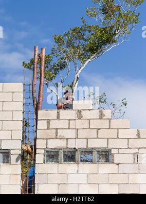 Maurerarbeiten: eine Mauer zu errichten. Maurer legt einen Betonblock hoch oben auf einer neu gebauten Betonklotz Mauer Stockfoto