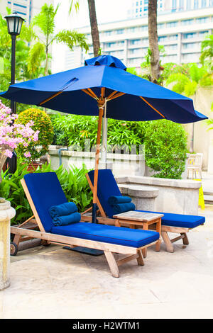 Zwei blaue Liegestühle mit Sonnenschirmen in der Nähe von Schwimmbad im Luxushotel Stockfoto