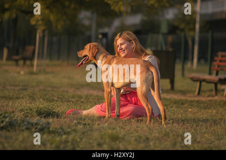 junge niedliche übergewichtige Frau sitzen im Rasen Hund Sonnentag Stockfoto