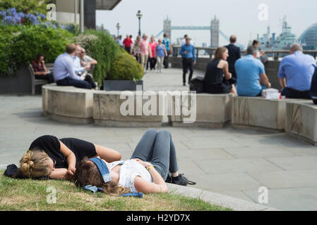 Schreibtischarbeiter machen ein Nickerchen, sitzen oder Essen an den Ufern der Themse vor Tower Bridge zur Mittagszeit, London, UK Stockfoto